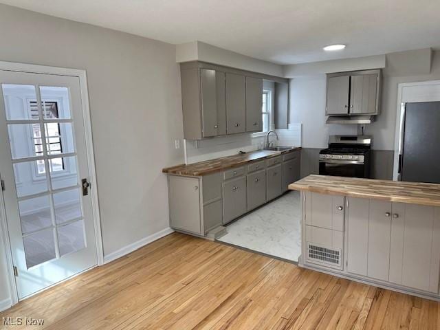 kitchen featuring stainless steel gas range oven, gray cabinetry, a sink, freestanding refrigerator, and light wood finished floors