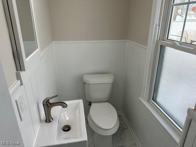 bathroom featuring marble finish floor, a wainscoted wall, a decorative wall, and toilet