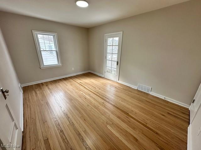 empty room with light wood-type flooring, visible vents, and baseboards