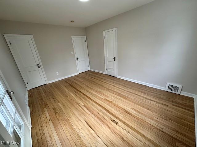 unfurnished bedroom with wood finished floors, visible vents, and baseboards