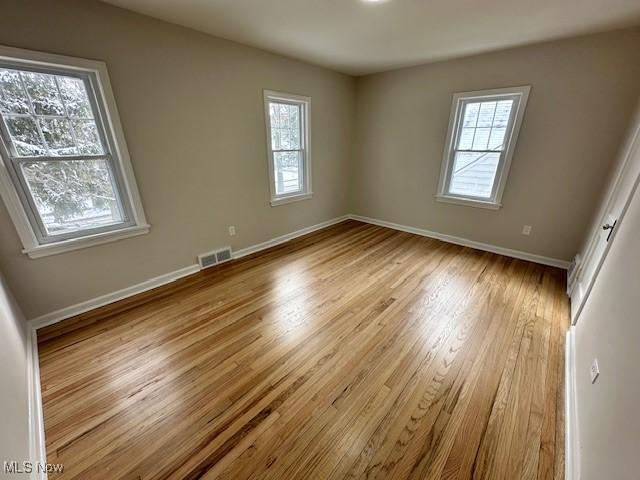 empty room with baseboards, plenty of natural light, visible vents, and wood finished floors