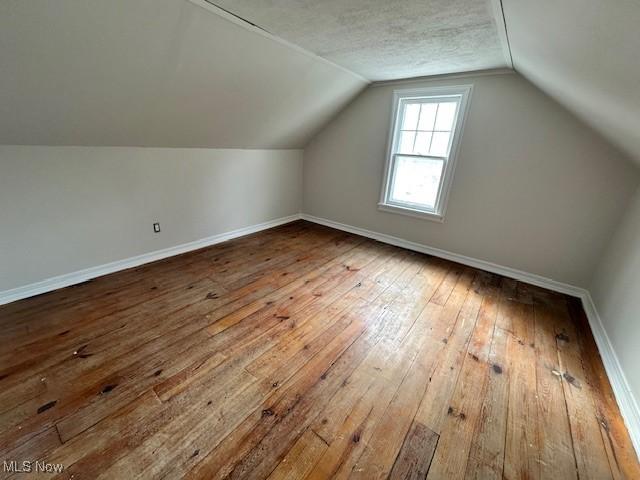 bonus room featuring lofted ceiling, baseboards, a textured ceiling, and hardwood / wood-style floors