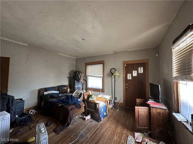 bedroom featuring radiator, wallpapered walls, baseboards, and wood finished floors