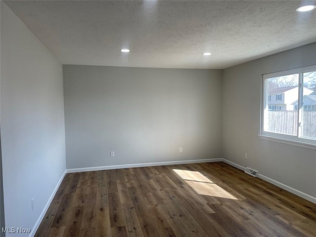 spare room with visible vents, dark wood finished floors, a textured ceiling, and baseboards