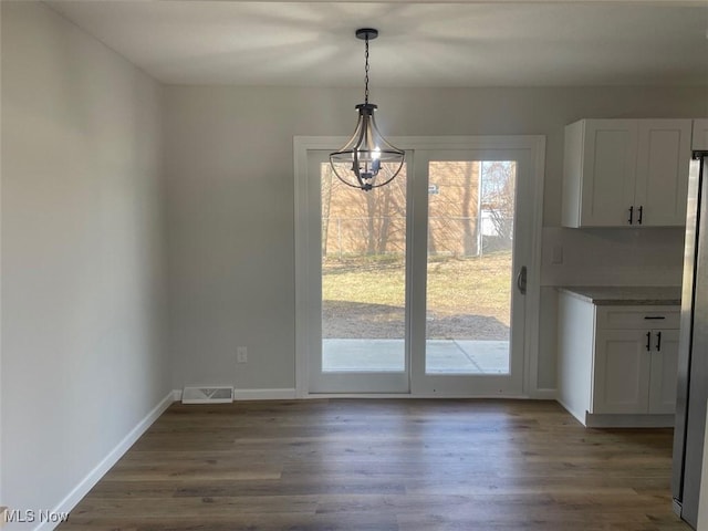 unfurnished dining area featuring an inviting chandelier, baseboards, visible vents, and wood finished floors