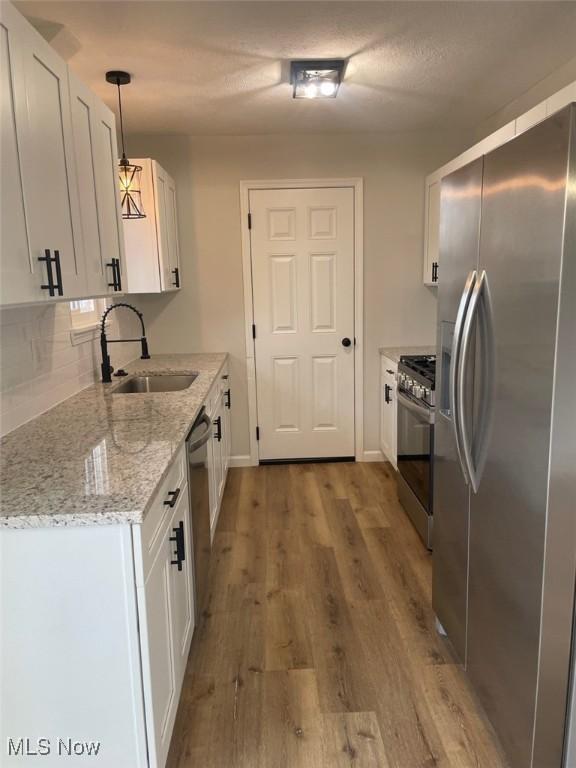 kitchen with stainless steel appliances, wood finished floors, white cabinets, a sink, and light stone countertops