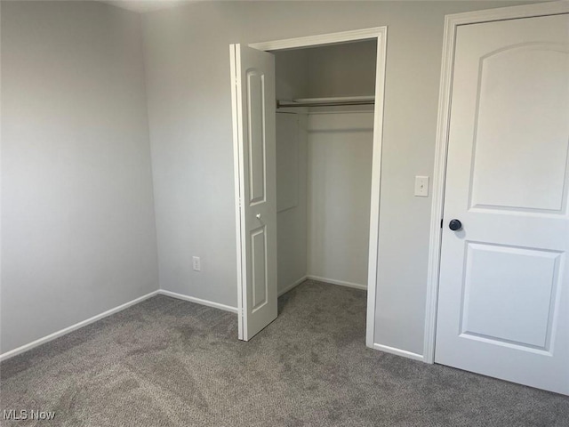 unfurnished bedroom featuring dark colored carpet, a closet, and baseboards