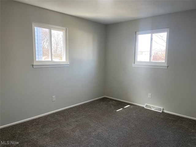 empty room with baseboards, visible vents, and dark carpet