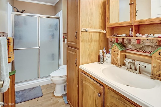 bathroom featuring toilet, wood finished floors, crown molding, vanity, and a shower stall