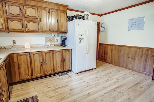 kitchen with white fridge with ice dispenser, brown cabinets, crown molding, and wainscoting