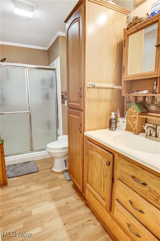 full bathroom with toilet, wood finished floors, crown molding, vanity, and a shower stall