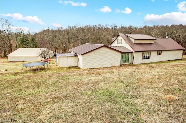 rear view of house featuring a forest view, metal roof, a lawn, and an outbuilding