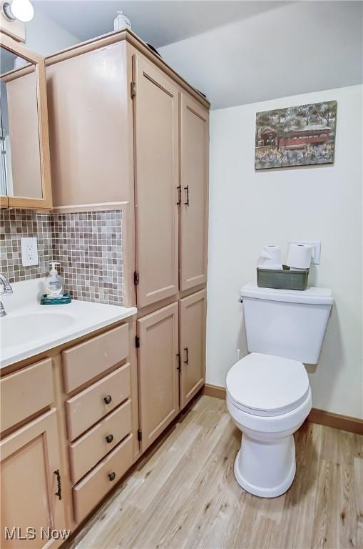 half bath with toilet, wood finished floors, vanity, baseboards, and backsplash