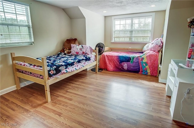 bedroom with vaulted ceiling, a textured ceiling, baseboards, and wood finished floors