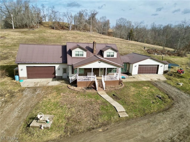 view of front facade featuring metal roof, covered porch, a garage, driveway, and a front lawn