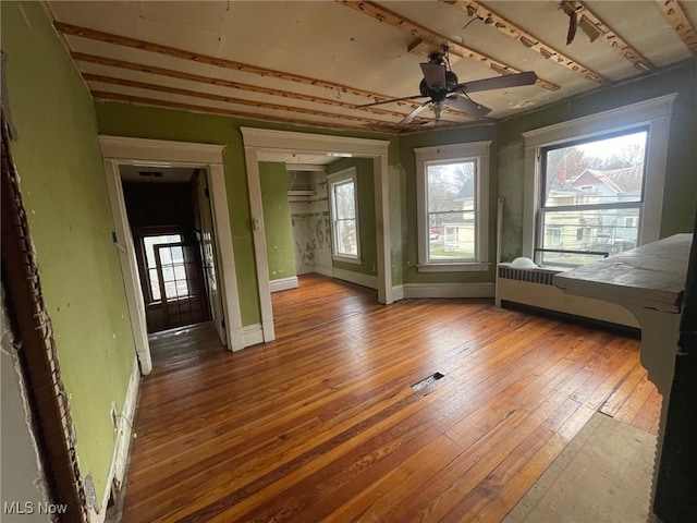 interior space with radiator heating unit, wood-type flooring, a ceiling fan, and baseboards