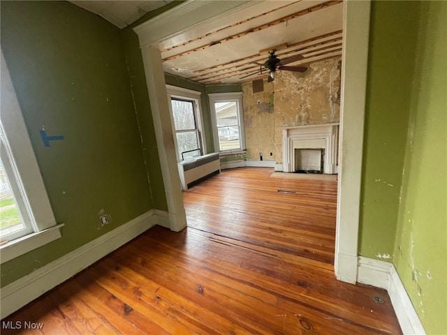 unfurnished living room featuring baseboards, radiator, wood-type flooring, ceiling fan, and a fireplace