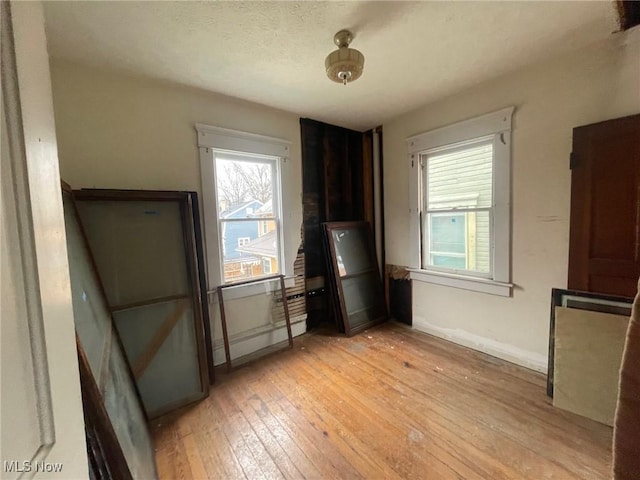 interior space with light wood-type flooring, a textured ceiling, and baseboards