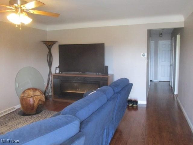 living room with visible vents, a ceiling fan, a glass covered fireplace, wood finished floors, and baseboards