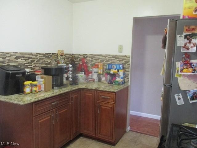 kitchen with light tile patterned floors, light stone counters, backsplash, and freestanding refrigerator