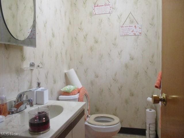 half bathroom featuring vanity, toilet, and wallpapered walls