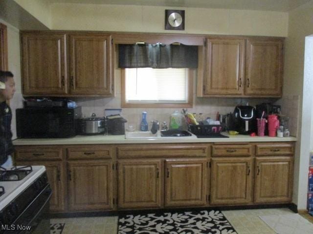 kitchen featuring brown cabinetry, light countertops, light floors, a sink, and gas stove