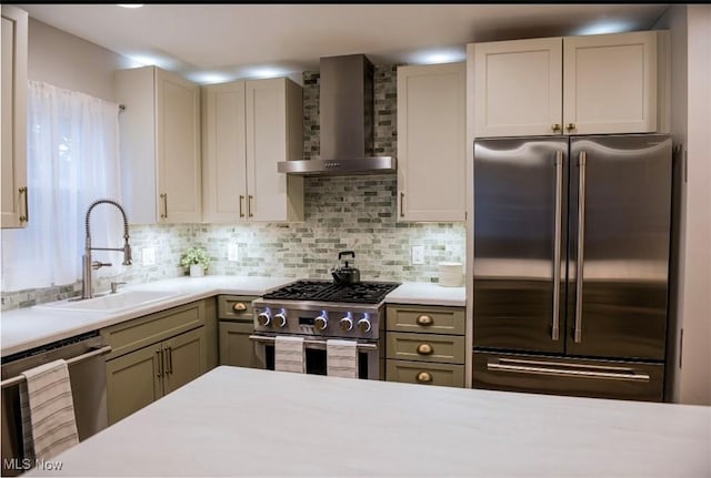 kitchen with premium appliances, tasteful backsplash, light countertops, a sink, and wall chimney range hood