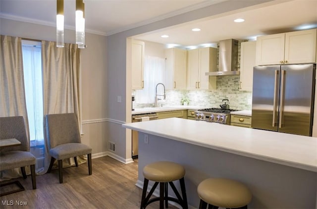 kitchen featuring a sink, light countertops, ornamental molding, wall chimney range hood, and appliances with stainless steel finishes