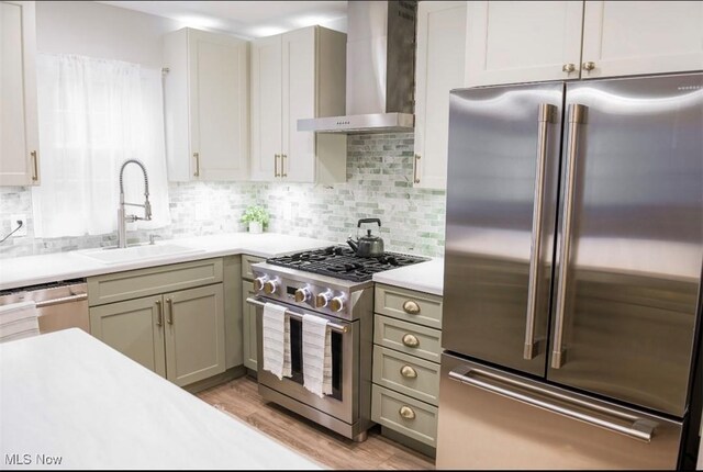 kitchen with high end appliances, wall chimney exhaust hood, light countertops, light wood-style floors, and a sink