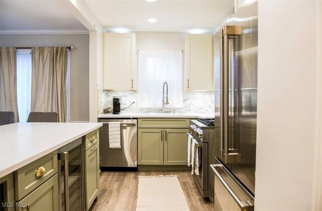 kitchen featuring premium appliances, beverage cooler, a sink, light countertops, and light wood-type flooring