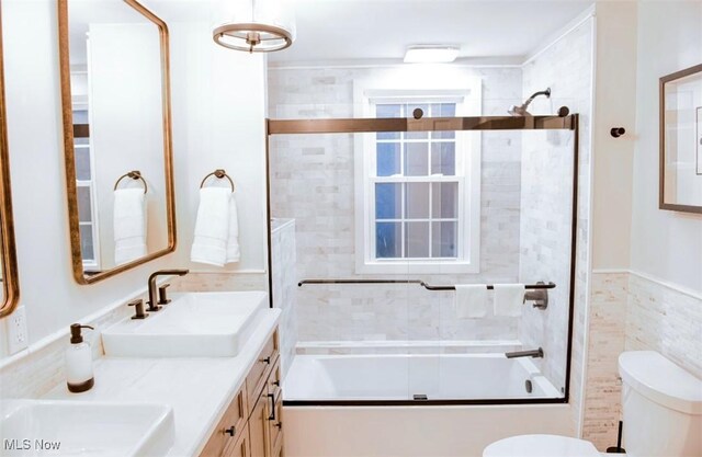 bathroom featuring toilet, double vanity, enclosed tub / shower combo, and a sink