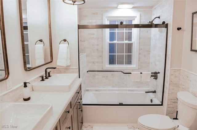 bathroom featuring combined bath / shower with glass door, a sink, tile walls, and toilet