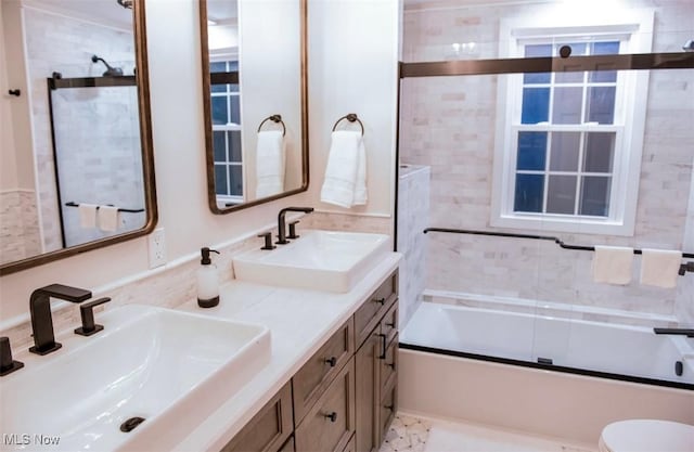 bathroom featuring shower / bath combination with glass door, a sink, toilet, and double vanity