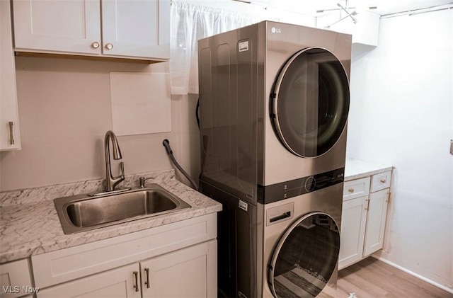 clothes washing area with light wood finished floors, stacked washer / dryer, a sink, and cabinet space