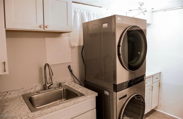 laundry room with light wood-type flooring, cabinet space, a sink, and stacked washing maching and dryer