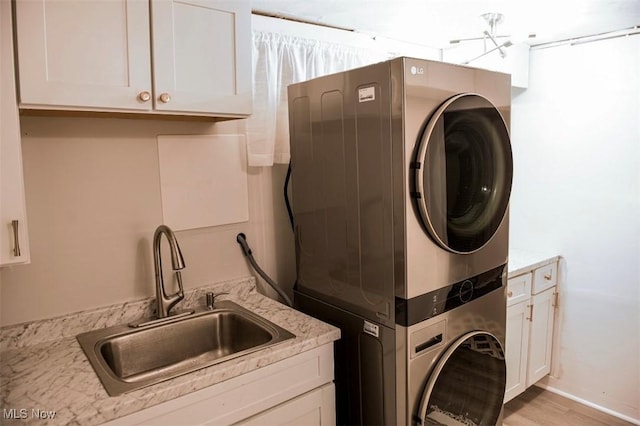 laundry area with stacked washer and clothes dryer, cabinet space, a sink, and light wood finished floors