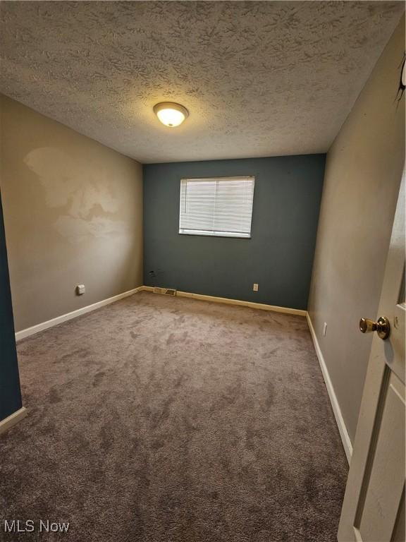 carpeted empty room featuring baseboards and a textured ceiling