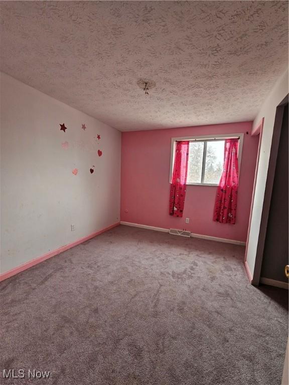 carpeted spare room featuring visible vents, a textured ceiling, and baseboards