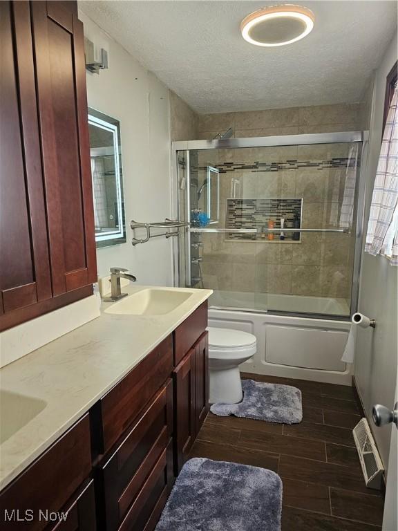 full bath featuring visible vents, toilet, a sink, enclosed tub / shower combo, and wood tiled floor