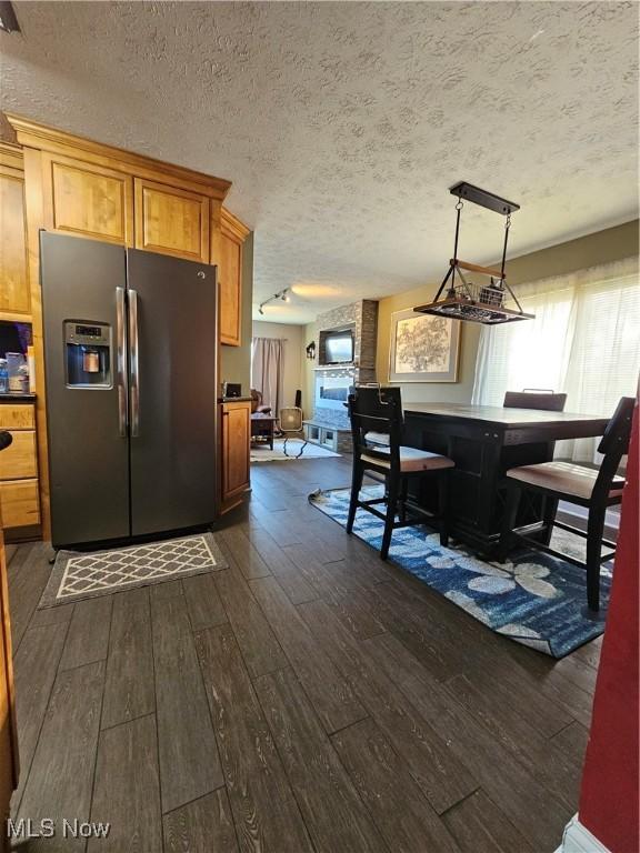 kitchen with brown cabinets, a textured ceiling, stainless steel refrigerator with ice dispenser, and dark wood-style flooring