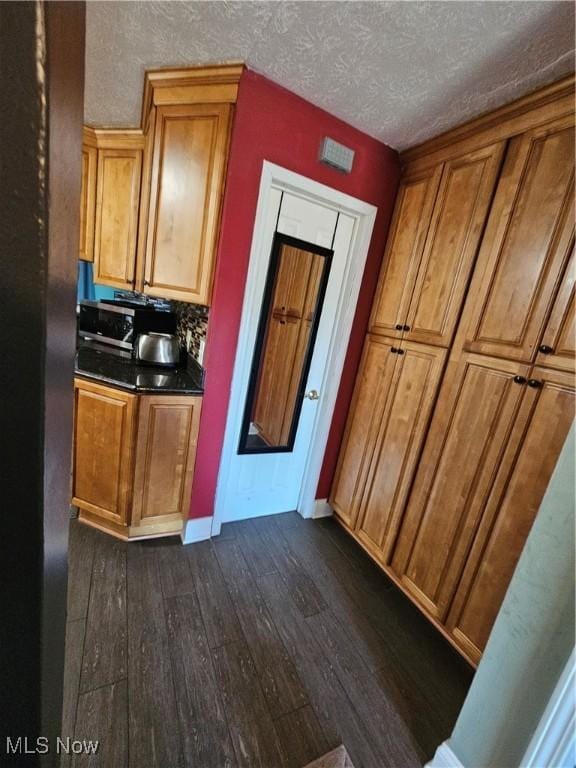 kitchen featuring dark wood-type flooring, dark countertops, brown cabinets, and a textured ceiling