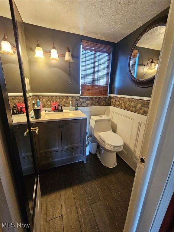 bathroom featuring a wainscoted wall, toilet, vanity, a textured ceiling, and wood-type flooring