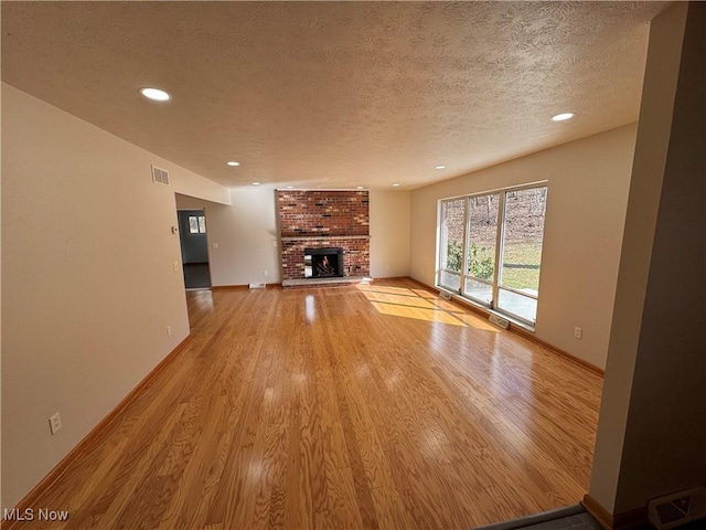 unfurnished living room featuring light wood-type flooring, a fireplace, visible vents, and a textured ceiling