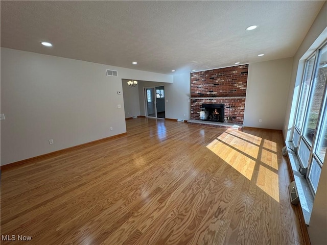 unfurnished living room with visible vents, a textured ceiling, baseboards, and wood finished floors