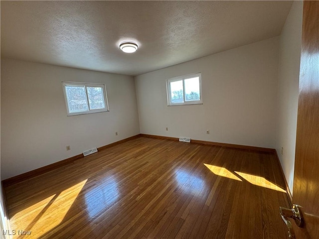 unfurnished room with a textured ceiling, hardwood / wood-style floors, visible vents, and baseboards