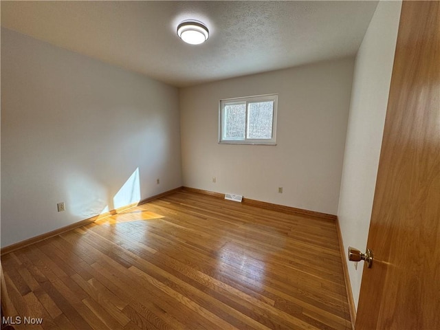 empty room featuring hardwood / wood-style flooring, baseboards, and visible vents