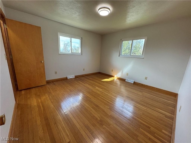 empty room featuring a wealth of natural light, visible vents, and light wood finished floors