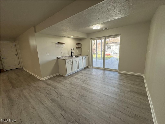 bar featuring a textured ceiling, a sink, visible vents, baseboards, and light wood-style floors