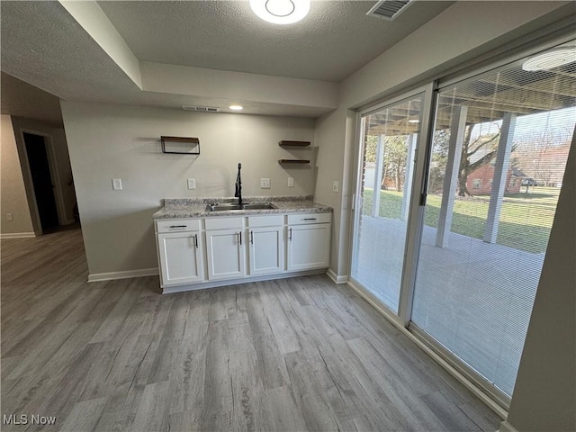 bar with baseboards, visible vents, a textured ceiling, light wood-style floors, and a sink