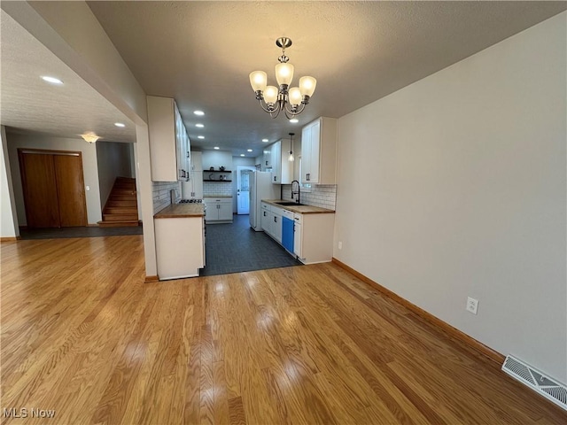 kitchen featuring tasteful backsplash, visible vents, white cabinets, a sink, and wood finished floors